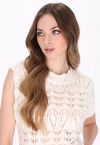 Strickpullover, offenes Spitzenmuster in Creme. Hoher Kragen, ärmellos. Sanfte Textur mit einem Muster aus Rauten und Zickzacken.