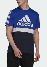 Camiseta de manga corta azul y azul marino con logotipo blanco y patrón de bloques de color horizontal; presenta tres franjas blancas en los hombros.
