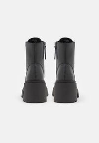 Bottes plates-formes en cuir noir avec fermetures éclair latérales vues de dos, montrant des semelles épaisses et des talons blocs.