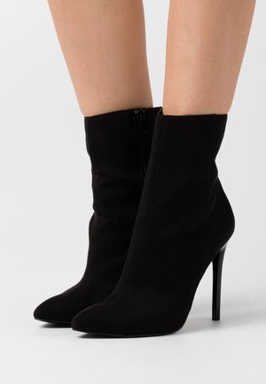 Stivaletti neri in suede con punta affusolata e tacco a stiletto alto; presentano una cerniera laterale per una facile vestibilità e una texture liscia e opaca.