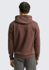 Bruine hoodie met een gestructureerde afwerking, aansluitende manchetten en zoom. Opvallende kenmerken zijn de kangoeroezak en de trekkoordkap.