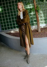 Olivengrön ylleblandad kappa med stora knappar, lagd över en brun kjol med en sidoflik, i kombination med grå ankelboots.