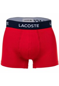 Piros pamut boxer alsónemű, sötétkék rugalmas derékpánttal, amelyen fehér "LACOSTE" logó található. Klasszikus szabás, varrott részletekkel.