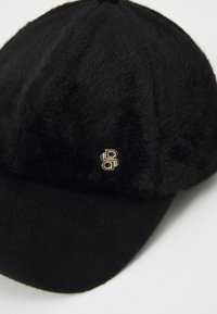 Mustmust kohe, millel on sile tekstuur ja ümar kroon. Esiküljel on kuldne logo ja kumer visor.
