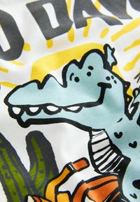 Bomulds T-shirt med et tegneseriealligators design i lyseblå, med sorte konturer, gule accenter og grønne kaktusillustrationer.