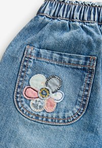 Tissu en denim avec une ceinture froncée et une poche arrière ornée d'une fleur patchwork multicolore avec un centre pailleté.