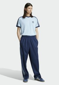 Camiseta de algodón azul claro con detalles y logo en navy, combinada con pantalones de chándal navy que presentan rayas blancas y cintura elástica.