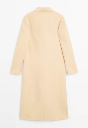 Kabát krémové barvy s výstřihem do V, dlouhými rukávy a rovný střihem. Má boční rozparky a čisté švy. Hladký materiál z vlněné směsi.