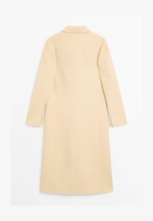 Kabát krémové barvy s výstřihem do V, dlouhými rukávy a rovný střihem. Má boční rozparky a čisté švy. Hladký materiál z vlněné směsi.