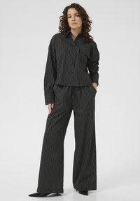 Black and white pinstripe button-up shirt and wide-leg pants set, featuring a chest pocket and relaxed fit. Smooth fabric with subtle sheen.