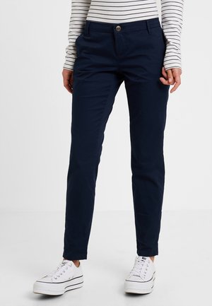 Granatowe chinosy o prostym kroju, z zapinaniem na guzik z przodu, szlufkami na pasek oraz gładką bawełnianą fakturą, połączone z białymi adidasami.