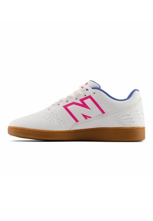 Hvid sneaker i lav model med gummisål, lyserødt kontureret "N"-logo, blå innerforing og snørelukning, vinklet mod venstre på hvid baggrund.