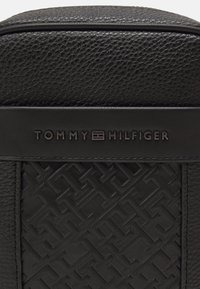 Borsa in pelle nera con superficie testurizzata e motivo impresso, con un prominente logo "TOMMY HILFIGER" in un carattere elegante e moderno.