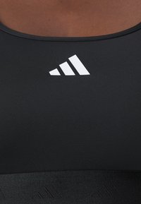 Black athletic tank top with smooth, stretchy fabric. Features white brand logo and tonal accent patterns on the waistband.