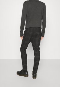 Zwarte geruite broek met een getailleerde pasvorm, voorzien van een subtiel ruitpatroon en een strakke textuur, gecombineerd met zwarte leren schoenen.