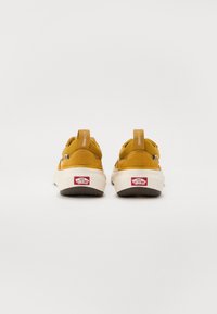 Gelbe Wildledersneaker mit einer weißen Gummisohle, ausgestattet mit einem Ziehhilfe und Branding auf der Rückseite. Abgerundete Form und strukturierte Akzente.