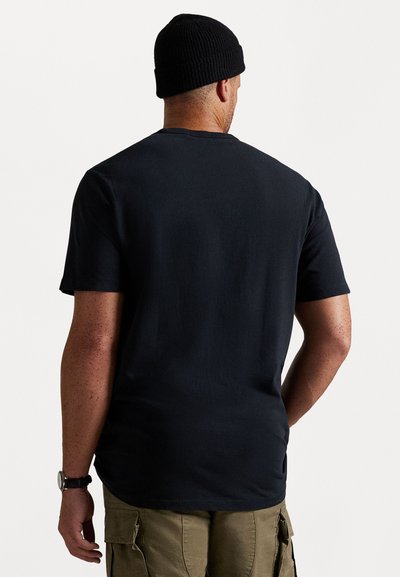 Melnas īsām piedurknēm T-krekls ar apaļu izgriezumu, gluda tekstūra un minimālistisks dizains. Valkāts ar beigu krāsas biksēm un melnu adītu beanie cepuri.