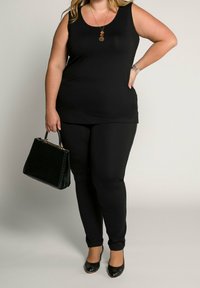 Top negro sin mangas y leggings negros, combinados con un bolso negro. El top es suave, mientras que los leggings tienen una textura ajustada. Zapatillas negras.