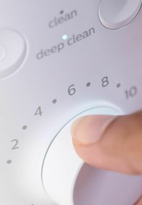 De controleknop, wit met een gladde afwerking, heeft nummers van 2 tot 10, en is voorzien van etiketten voor "schoon" en "diepe reiniging," met een vinger die de knop verstel.