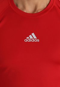 Rode sportieve shirt gemaakt van glad, rekbaar materiaal. Heeft een ronde halslijn en een wit Adidas-logo op de borst.