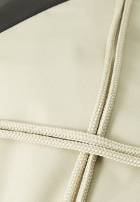 Tissu beige avec une texture lisse, featuring des accents en corde blanche tissée disposés en motif croisé. Inclut une section en cuir marron foncé.