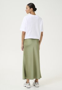Biely bavlnený tričko s krátkymi rukávmi v kombinácii s maxi sukňou z green saténu. K outfitu sú doplnené biele a strieborné tenisky.