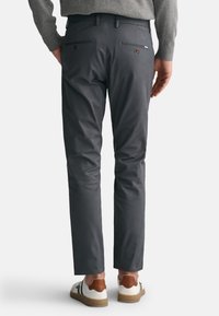 Grau melierte Baumwollmischung-Chinos mit schmalem Schnitt, ausgestattet mit Gesäßtaschen mit Knopfverschluss und einer glatten Textur, kombiniert mit lässigen Sneakern.