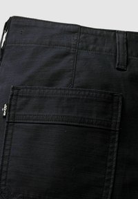 Pantalon en denim noir en gros plan montrant la poche arrière avec l’étiquette du logo Levi’s et un passant de ceinture sur un tissu texturé.