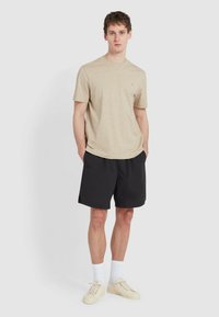 T-shirt beige a maniche corte con scollo rotondo, abbinato a pantaloni sportivi neri. Indossato con calzini bianchi e sneakers di colore chiaro.
