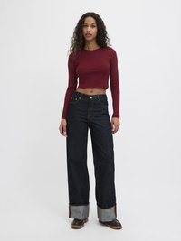 Beskarpet burgunder langermet topp kombinert med vide mørke denimjeans som har kontrasterende lyse denimmansjetter og synlige sømmer.