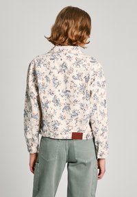 Denimjakke med blomstermønster i lys kremfarge, blå paisleymotiver og små fargerike blomster. Har en lærlogo på baksiden.