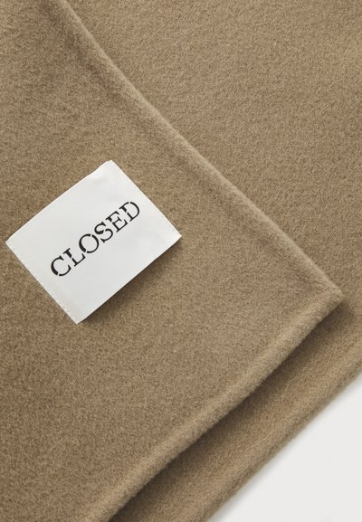 Bufanda de lana beige con textura suave, que presenta una etiqueta blanca prominente con el texto negro "CLOSED." Bordes suaves y diseño minimalista.
