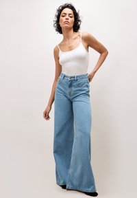 Jean taille haute à jambes larges en denim bleu clair. Comprend des poches avant, des poches arrière et une fermeture à bouton avec une braguette zippée.