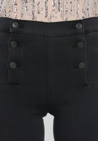 Pantalons noirs taille haute en tissu texturé, dotés d'une fermeture à bouton et de détails de boutons décoratifs à l'avant.