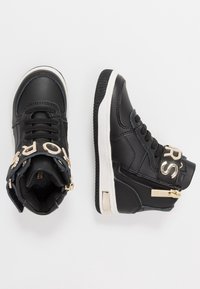 Černé kožené vysoké tenisky s kovovými zlatými prvky a zipy, s bílou gumovou podrážkou a texturovanými akcenty.