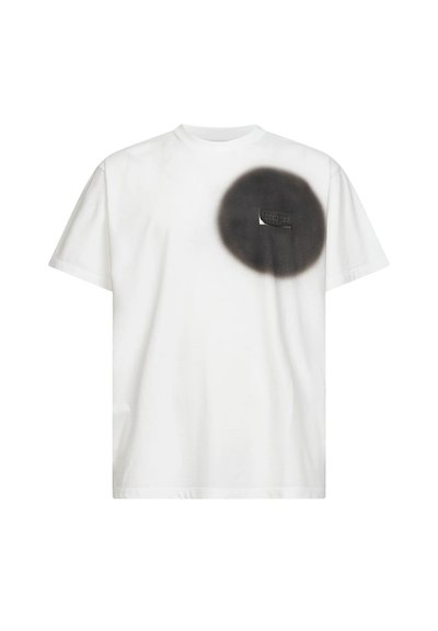 T-shirt blanc à manches courtes avec un cercle noir au pochoir sur le côté gauche de la poitrine et une petite poche partiellement visible à l'intérieur du cercle.