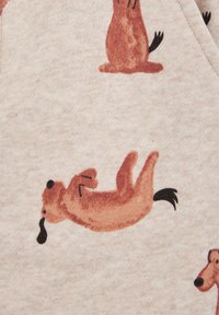 Beige audums ar atkārtotu rakstu, kurā redzami rotaļīgi, karikatūras stila suņi oranžā un brūnā krāsā, ar melniem akcentiem acīm un astēm.