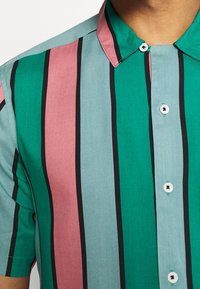 Camicia a maniche corte con righe verticali in teal, rosa e grigio. Presenta un colletto button-down e righe di accento nere. Tessuto dalla texture liscia.