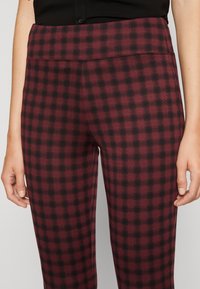 Legginsy w kratę w czerwono-czarnym kolorze o gładkiej fakturze i szerokim pasie, charakteryzujące się dopasowanym krojem i brakiem widocznych szwów.