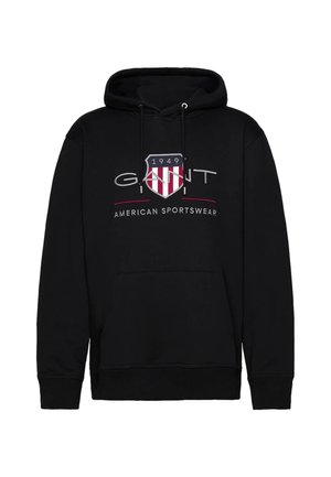 Black hooded sweatshirt with a front kangaroo pocket, featuring a white and red shield logo and “GANT AMERICAN SPORTSWEAR” text. Soft fabric.
