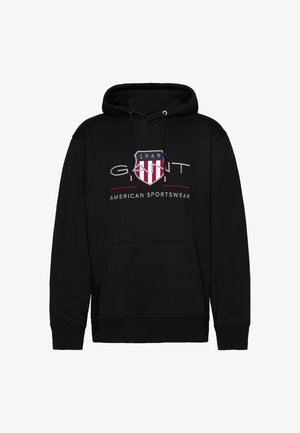 Černá mikina s kapucí a přední klokaní kapsou, s bílým a červeným štítovým logem a textem „GANT AMERICAN SPORTSWEAR“. Měkká tkanina.