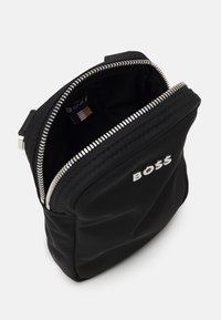 Borsa nera con zip e logo "BOSS" argento sulla parte anteriore, parzialmente aperta che mostra l'interno foderato in tessuto con un piccolo etichetta del marchio.