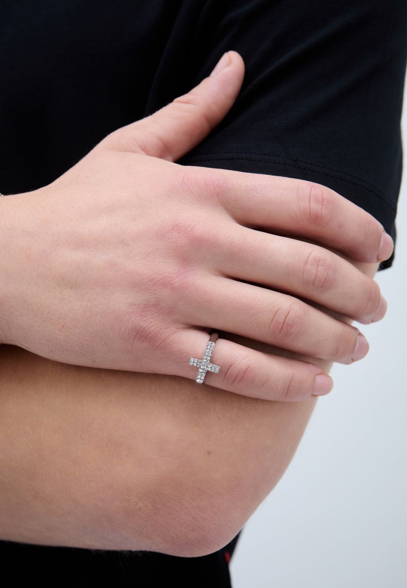 Hõbedane sõrmus, millel on ristmuster, kaunistatud selgete rhinestone'idega, kantud käel, mille taustal on must särk.