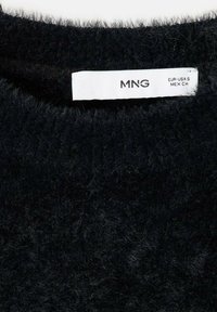 Cuello de suéter de punto negro y peludo con una etiqueta de cuidado blanca que muestra "MNG" e información de tallas. Textura suave y tejido suelto.