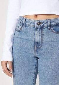 Höga blå denimjeans med en blekt finish, fem fickor, knappstängning och synliga söm detaljer.