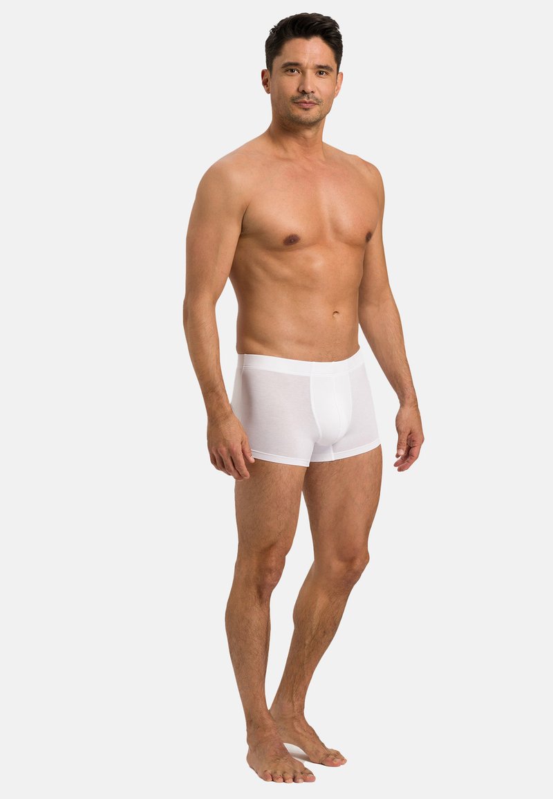 Vita bomullsboxer med en figurnära design. Slät textur, elastisk midjeband och inga synliga mönster. Modellen visas stående barfota.