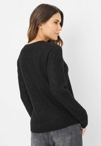 Schwarzer, gestrickter Pullover mit lockerer Passform, rundem Ausschnitt und verstreuten Glitzereffekten. Weiche Textur mit gerippten Bündchen.