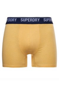 Heren gele katoenen boxershorts met een marineblauwe elastische tailleband met het "SUPERDRY" logo in het wit. Eenvoudige, gladde textuur en aansluitende pasvorm.