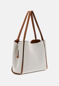 Sac fourre-tout en tissu gris clair avec des sangles en cuir marron et des finitions en cuir. Le design présente un dessus ouvert, un intérieur spacieux et une surface texturée.