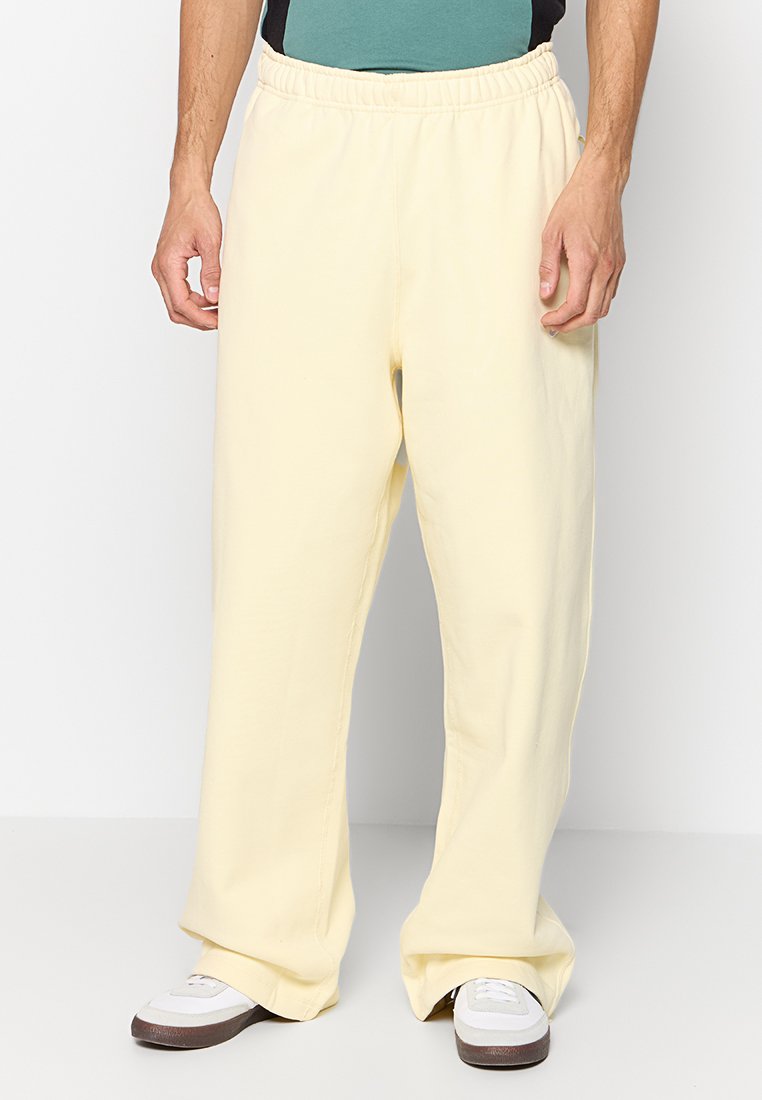 Pantalones de sudadera de algodón amarillos con un corte relajado, que presentan una cintura elástica y un dobladillo recortado. Llevados con zapatillas blancas.